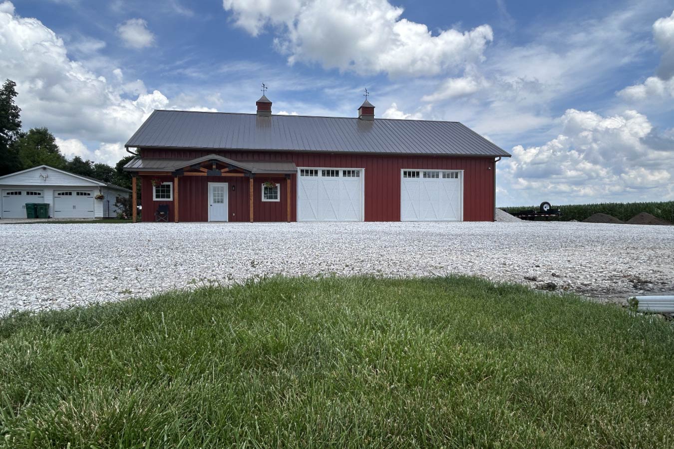 Residential workshop with red steel siding, steel roof, covered porch, and dual overhead doors