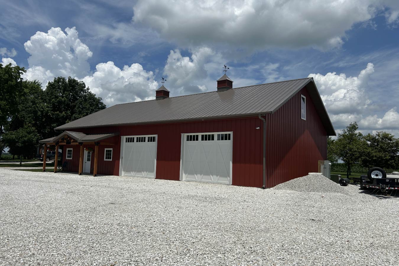 07-4676 Residential workshop with red steel siding, steel roof, dual overhead doors, and covered porch entrance