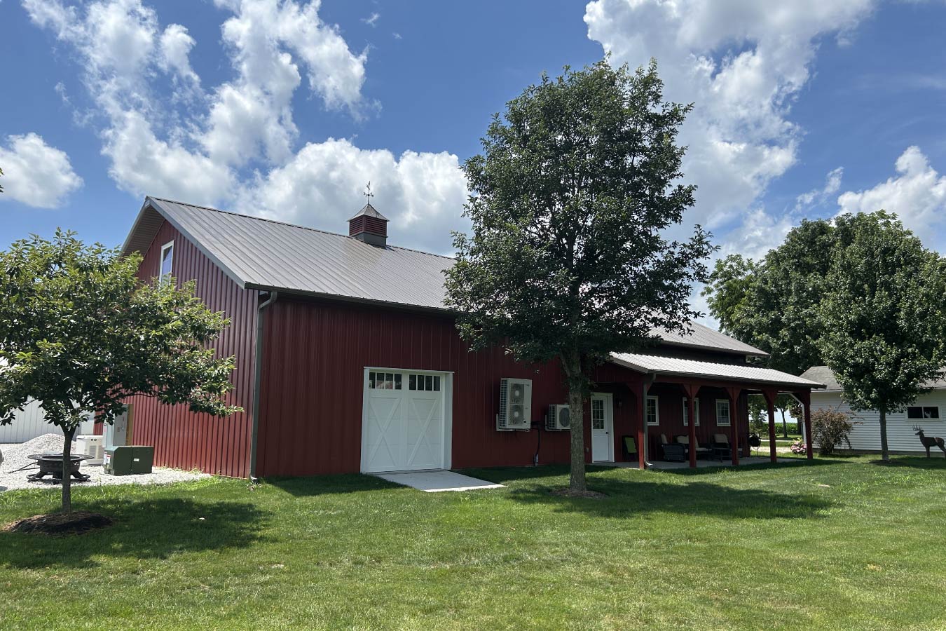Residential workshop with red steel siding, steel roof, covered porch, and single overhead door Rear access with 8′×8′ overhead door