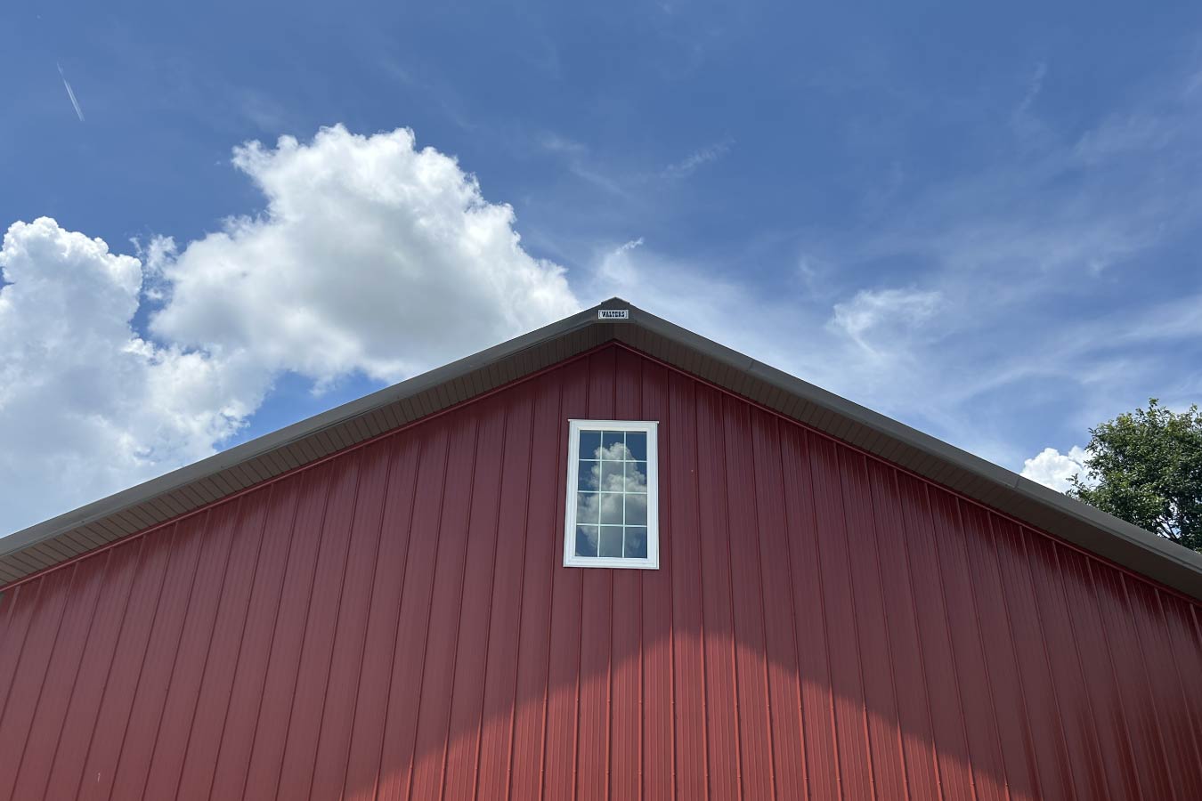 Residential workshop gable end with red steel siding and centered Plyco window