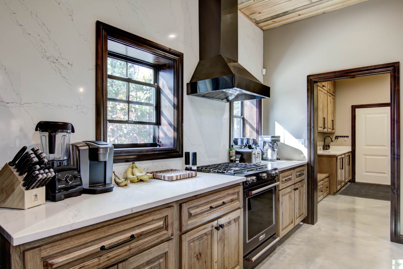 Barndominium kitchen with quartz countertops, wood cabinetry, and stainless range hood