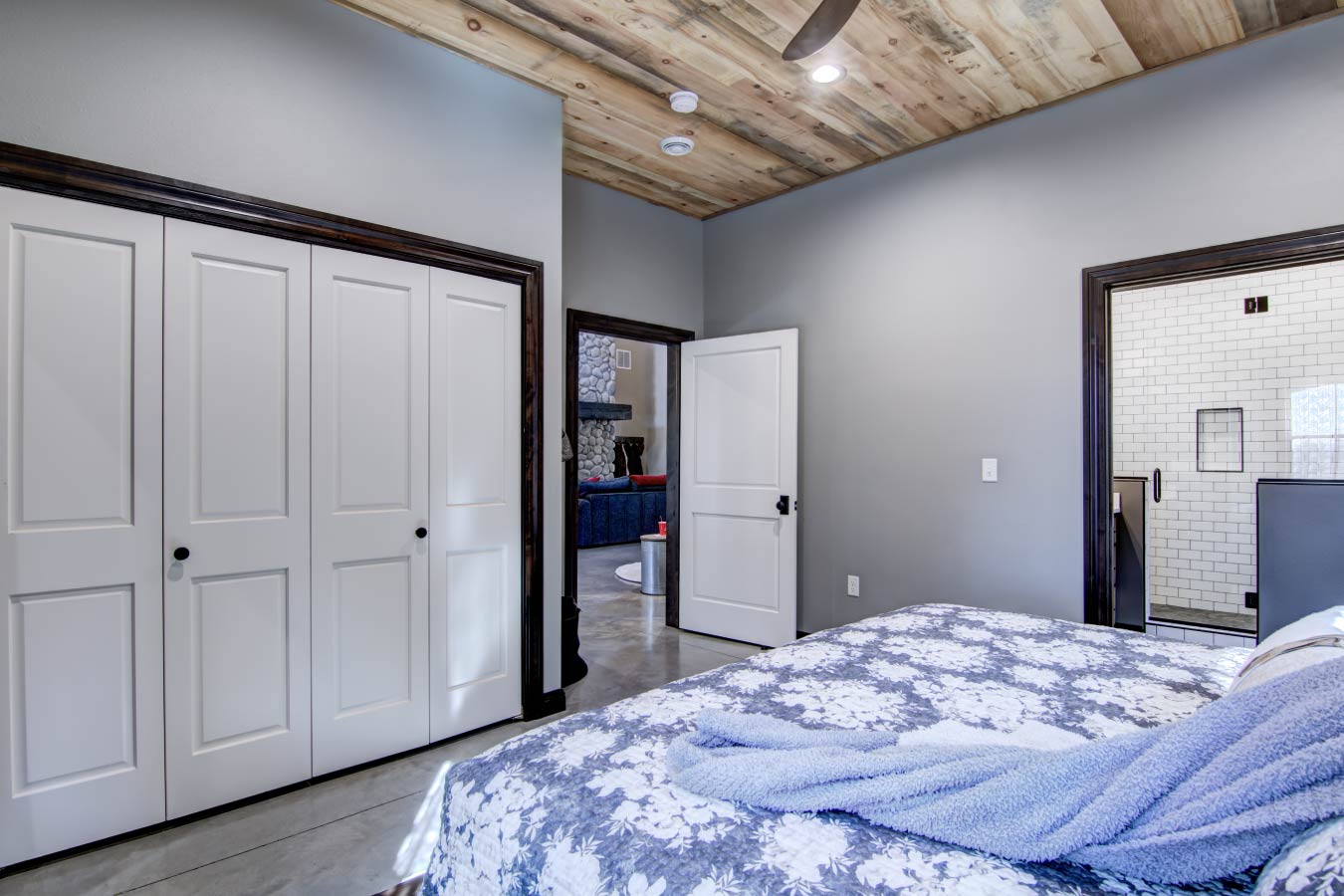 Barndominium bedroom with wood plank ceiling, closet doors, and attached bathroom