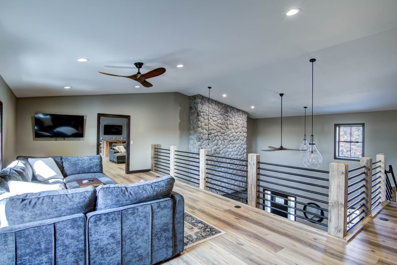 Barndominium loft living area with cable railing and stone fireplace wall