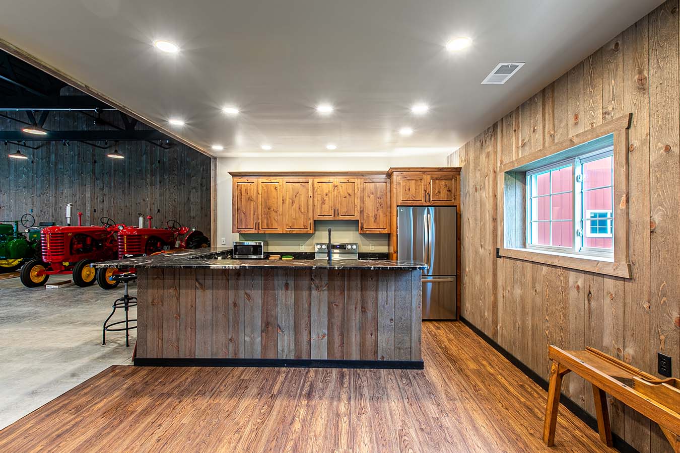 Pole barn interior with rustic kitchen, wood cabinetry, and vintage tractors in background
