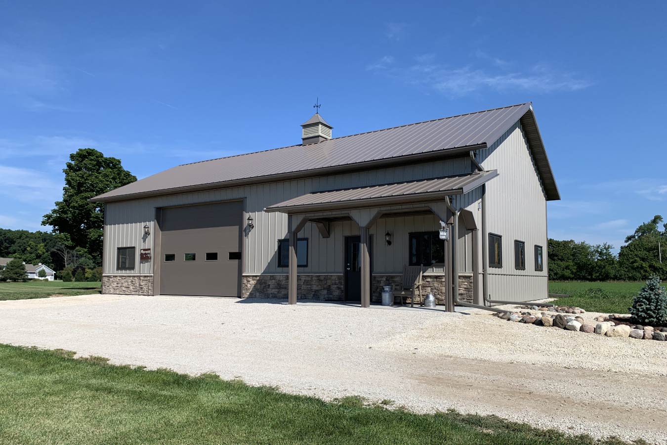 Residential workshop with steel siding, stone wainscot, overhead garage door, covered porch, and cupola