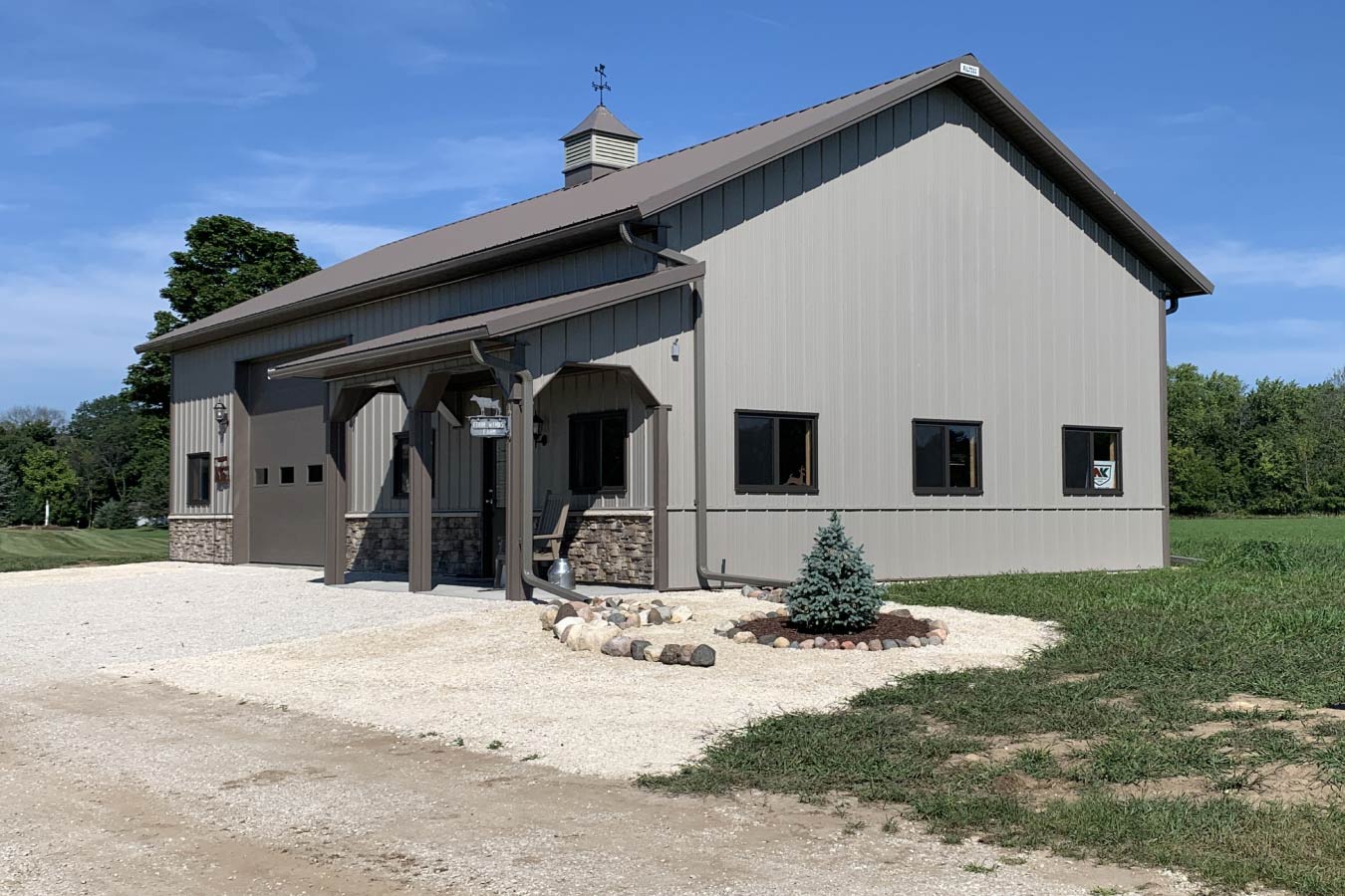 Residential workshop with steel siding, covered porch, stone wainscot, overhead garage door, and cupola