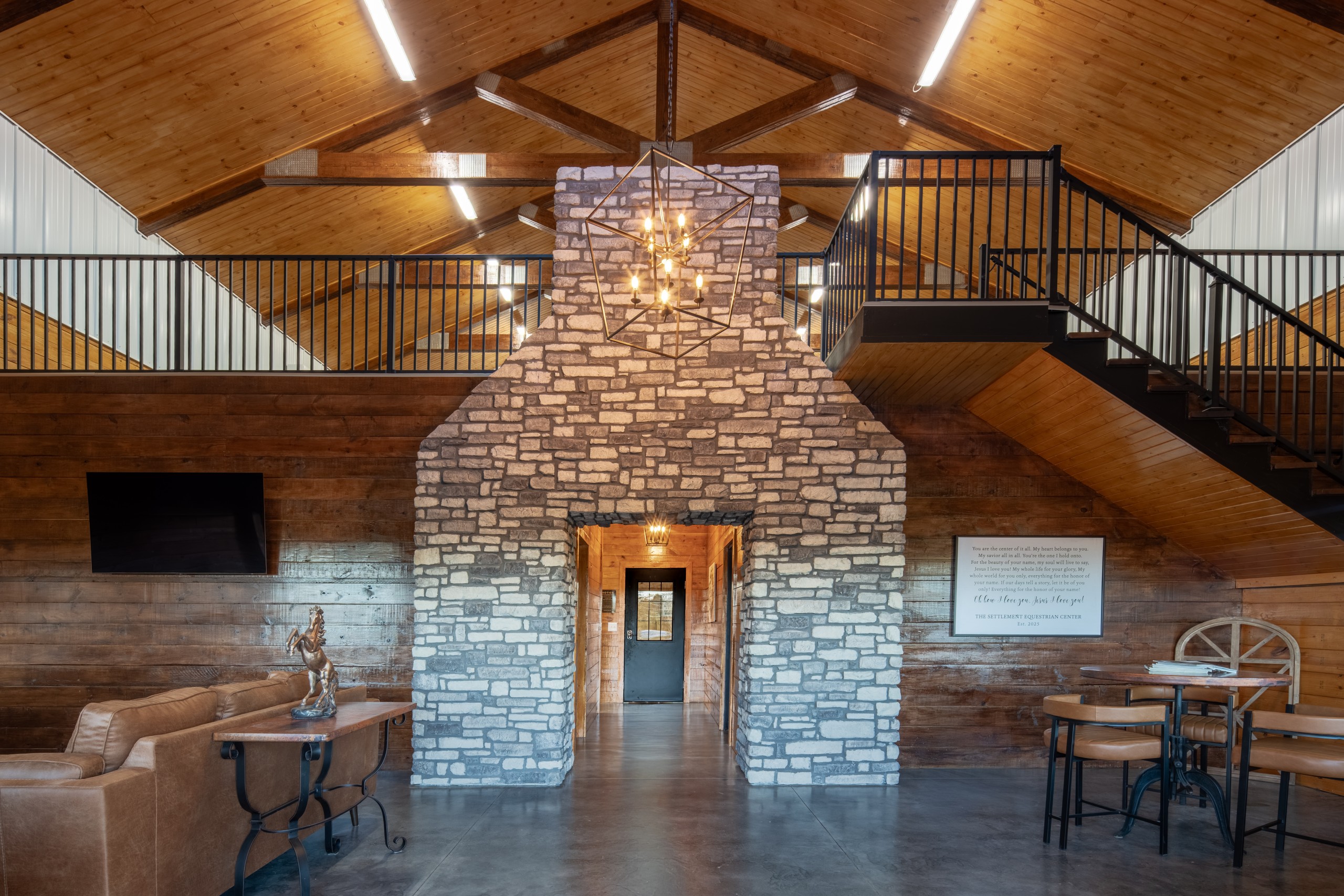 Lodge-style lobby at The Settlement Equestrian Center with stone feature wall, timber trusses, and upper-level balcony