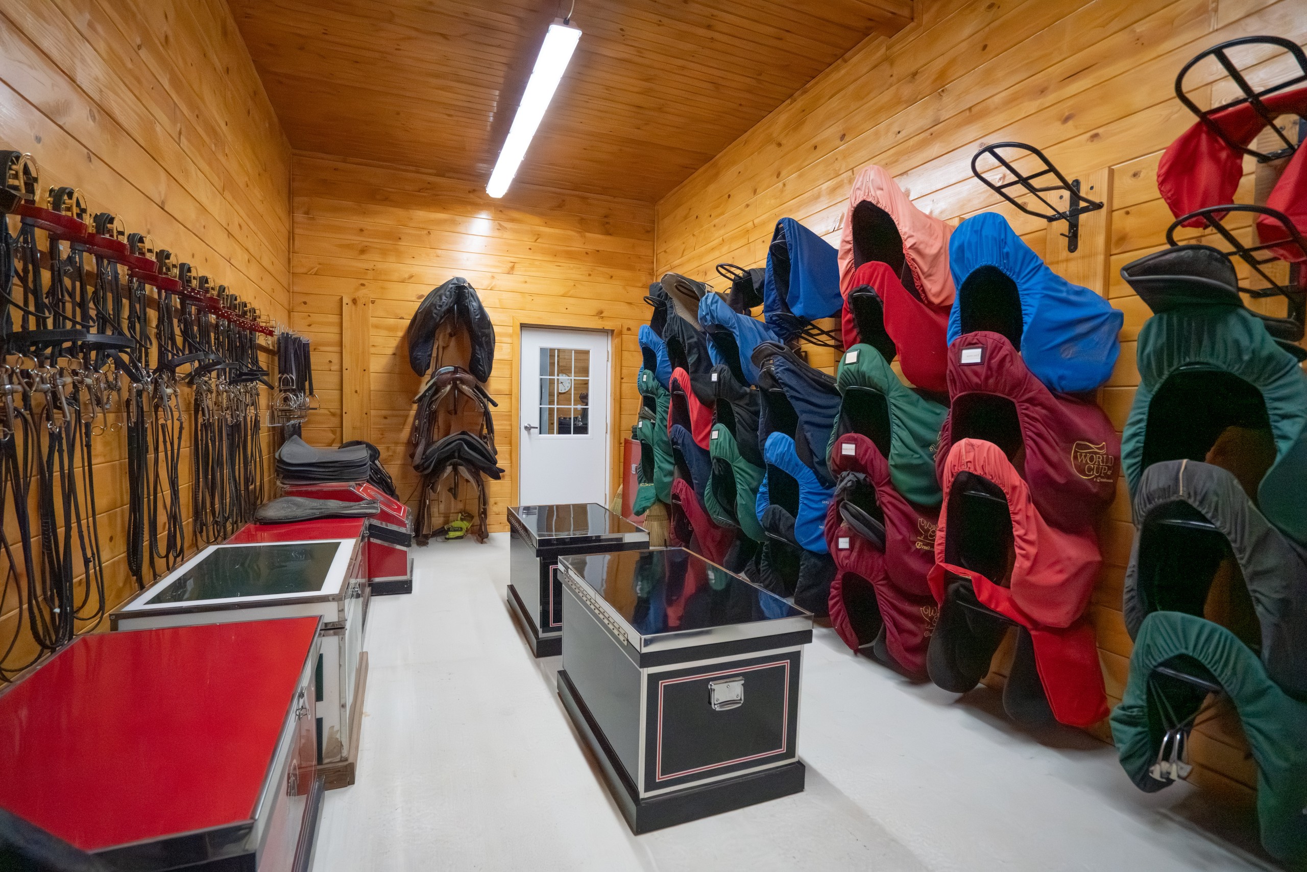 Tack room at The Settlement Equestrian Center with organized saddles, pads, tack storage, and wood interior finishes