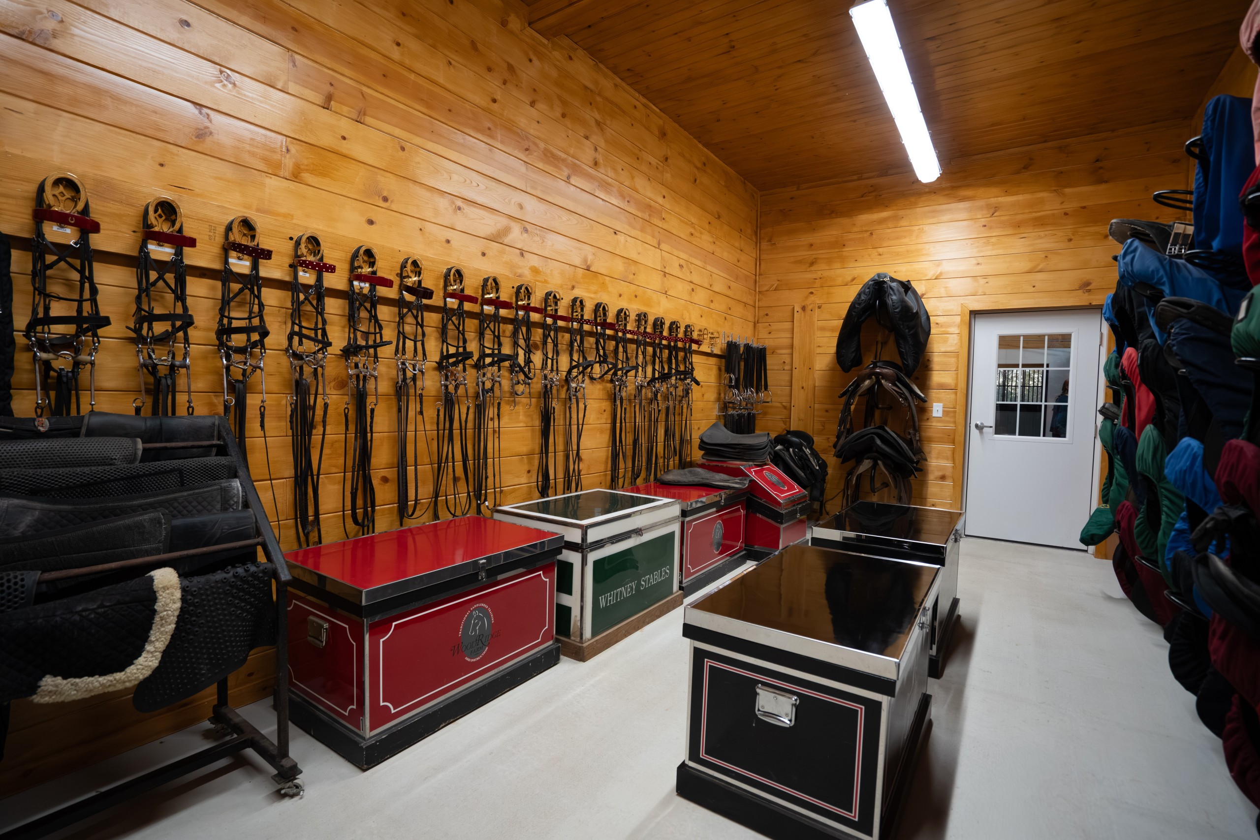 Organized tack room wall at The Settlement Equestrian Center with bridle racks, boot storage, and equestrian gear