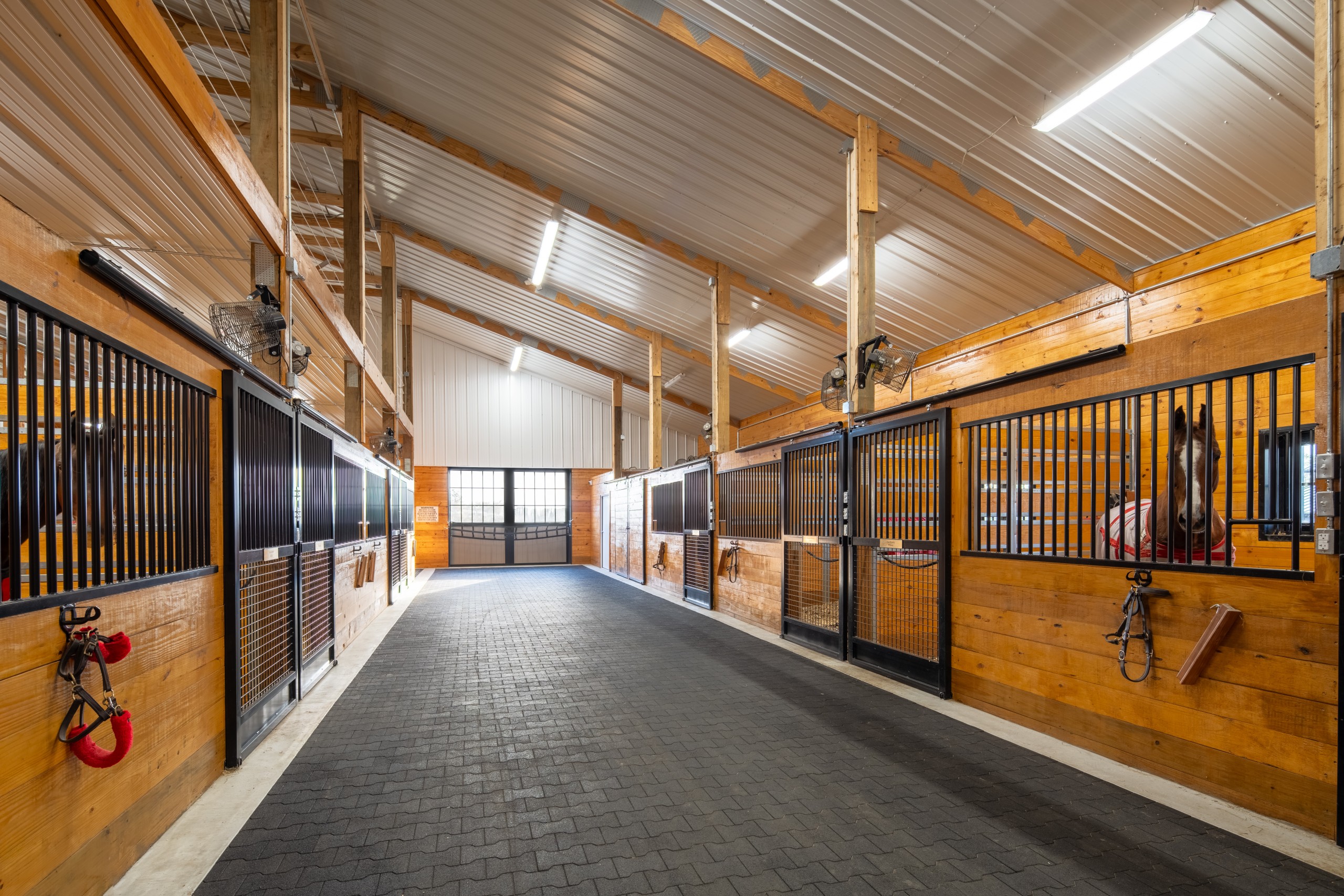Wide center aisle in the horse stall barn at The Settlement Equestrian Center with J&E Grill stall fronts and 24-stall layout