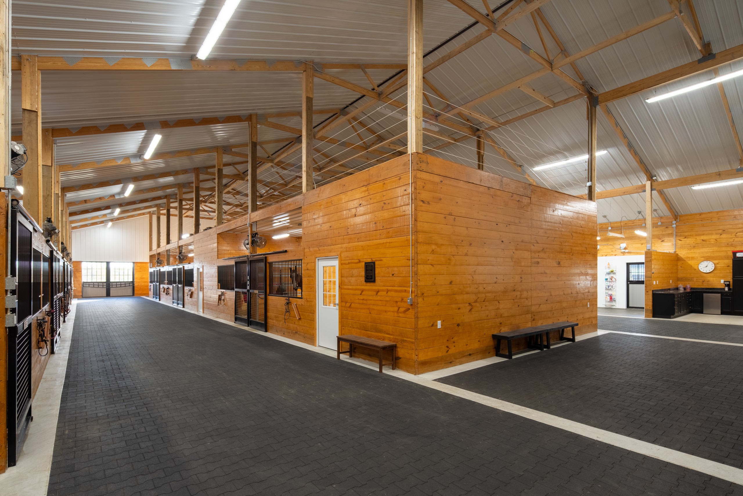 Center aisle inside the U-shaped horse stall barn at The Settlement Equestrian Center with premium J&E Grill stall fronts and wood-lined tack room walls