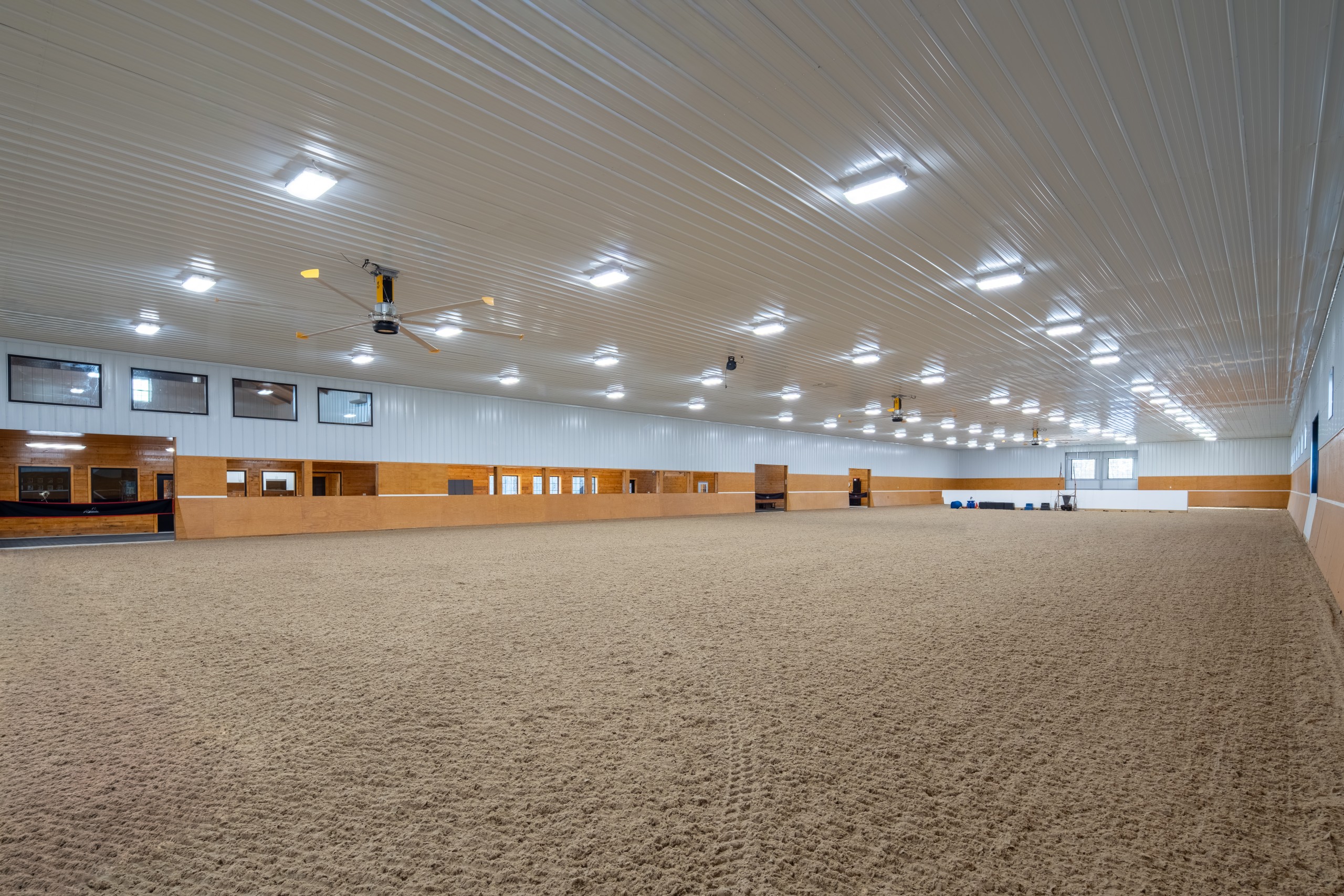 Lighted Indoor Riding Arena at The Settlement Equestrian Center Indoor riding arena at The Settlement Equestrian Center with bright overhead lighting, ceiling fans, and groomed equine footing