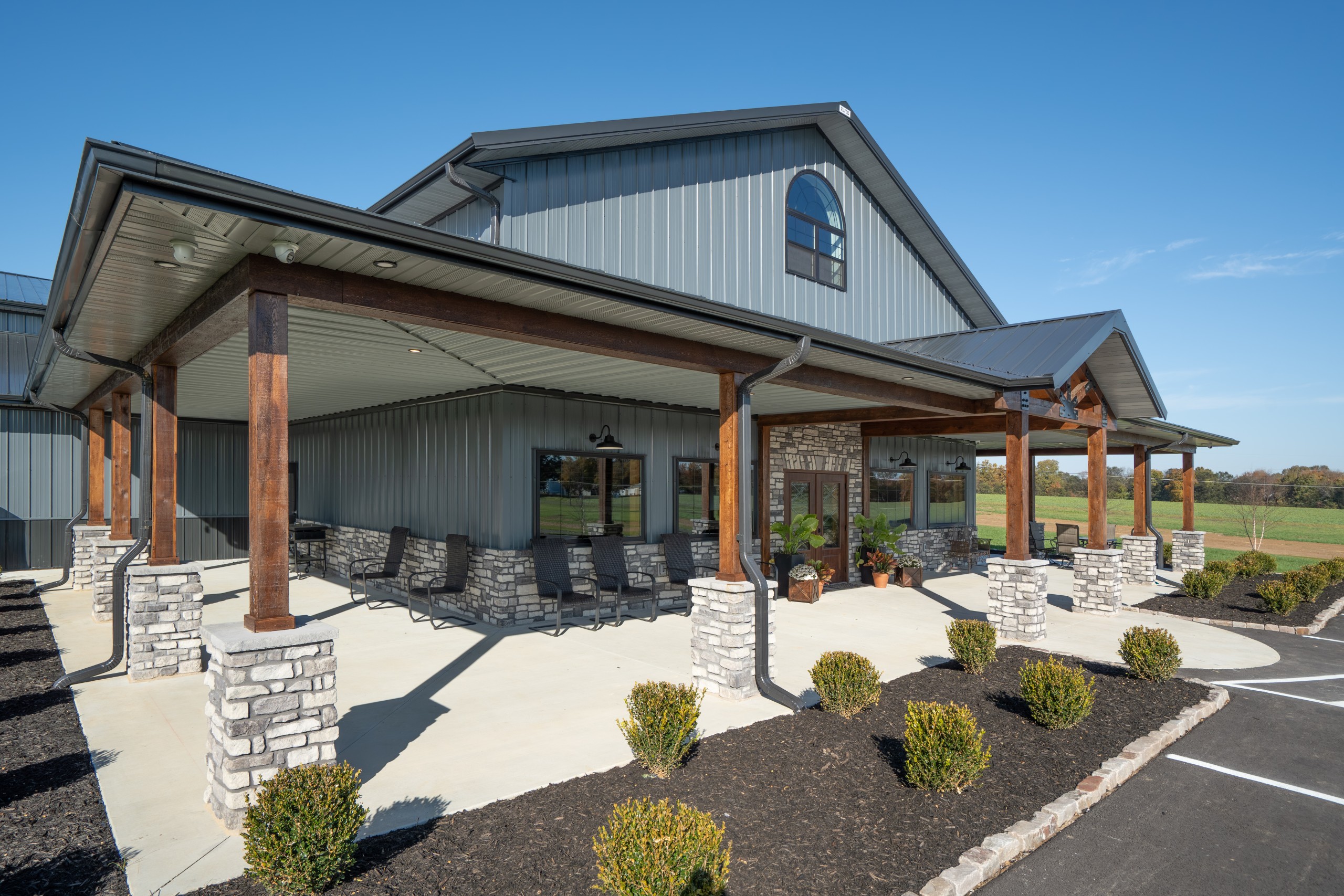 Angled exterior view of The Settlement Equestrian Center with covered porch, stone columns, and landscaped entrance