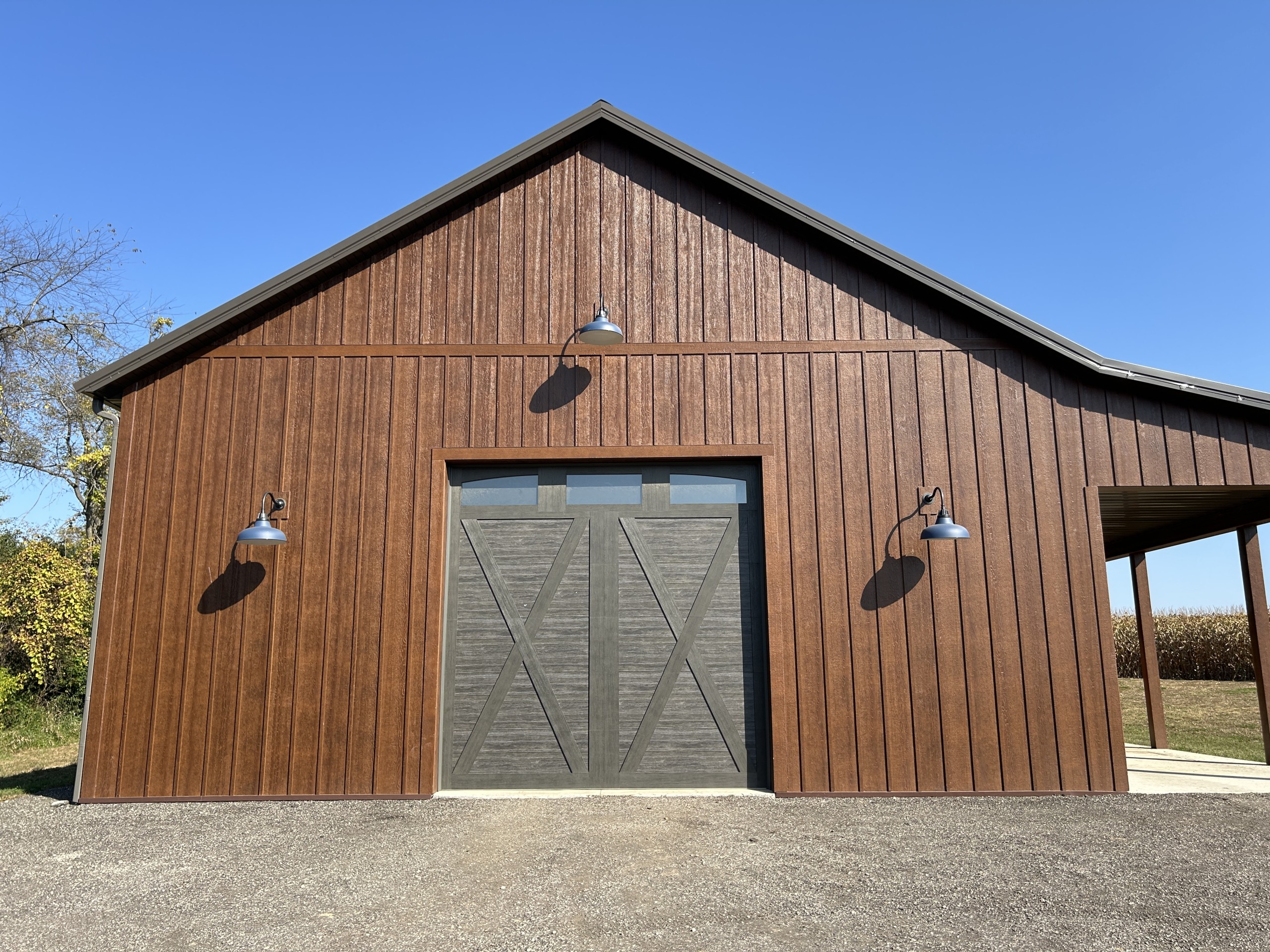 Front Elevation of 36′ x 72′ Board and Batten Workshop Front view of a 36' x 72' board and batten workshop with overhead door, gooseneck lights, and Burnished Slate roof