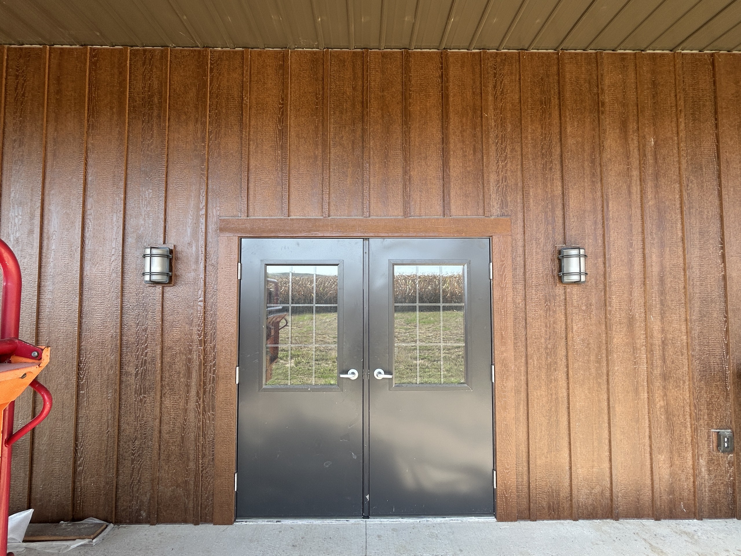 Dark bronze entry doors under the side porch of a 36' x 72' board and batten pole shed