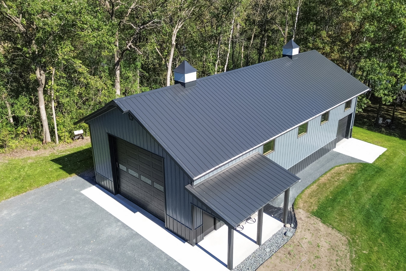 Rear view of black 30x64 post frame garage with vertical metal siding and gable roof in wooded setting