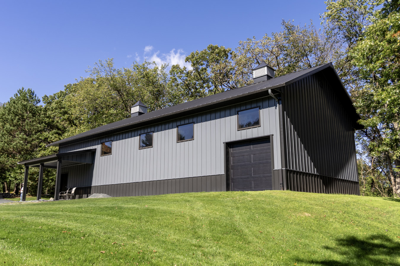 Angled aerial view of custom 30x64 garage with covered patio, black roof, and surrounding trees