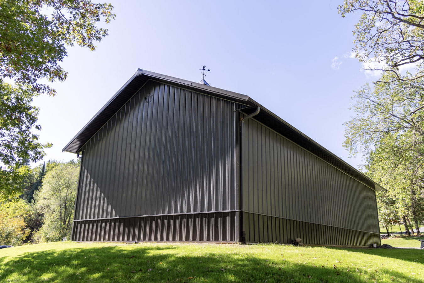 Custom 30x64 post frame garage with covered porch, black metal roof, and gray siding in natural setting