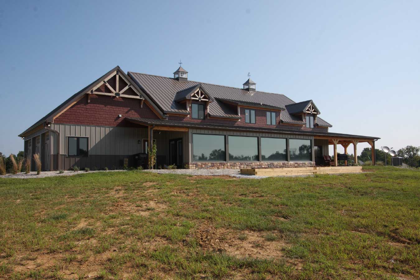 Rear view of luxury timber frame home with covered back porch and large windows overlooking the property.