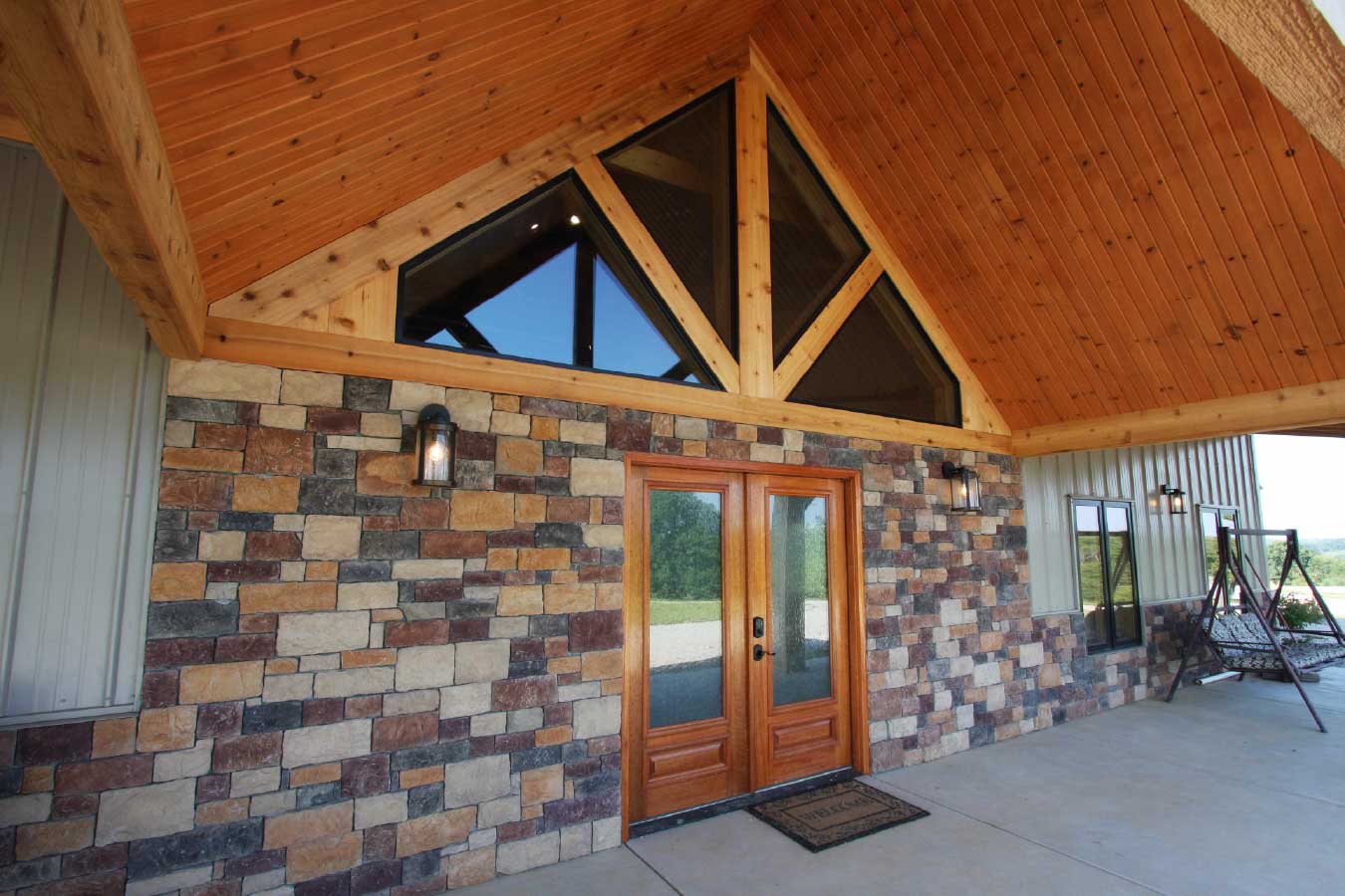 Main entrance of a luxury timber frame home in Kentucky featuring a decorative timber truss, large windows, and custom post-frame residential design.