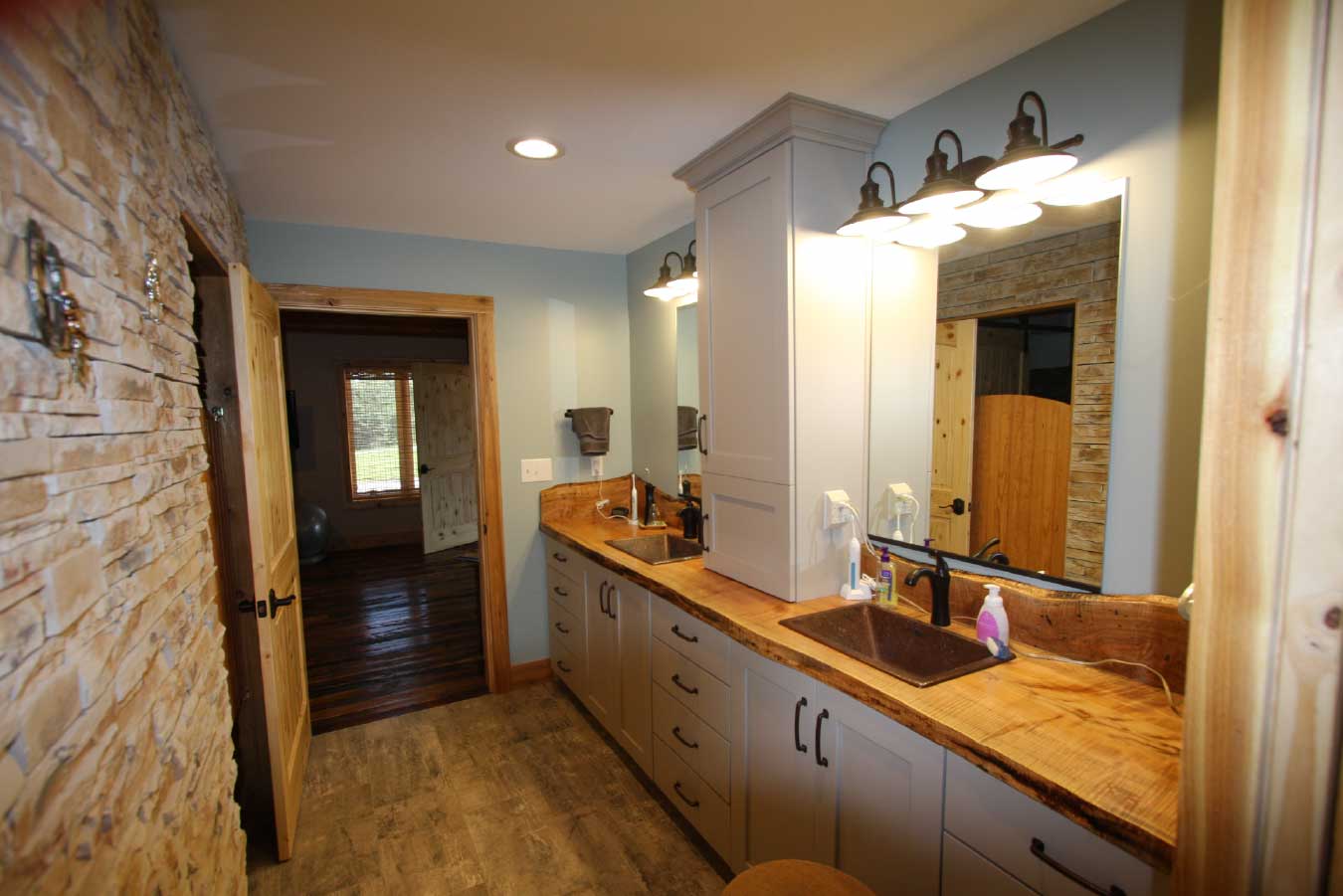 Bathroom inside a luxury timber frame home featuring a double vanity, wood countertop, stone accent wall, and rustic residential design.
