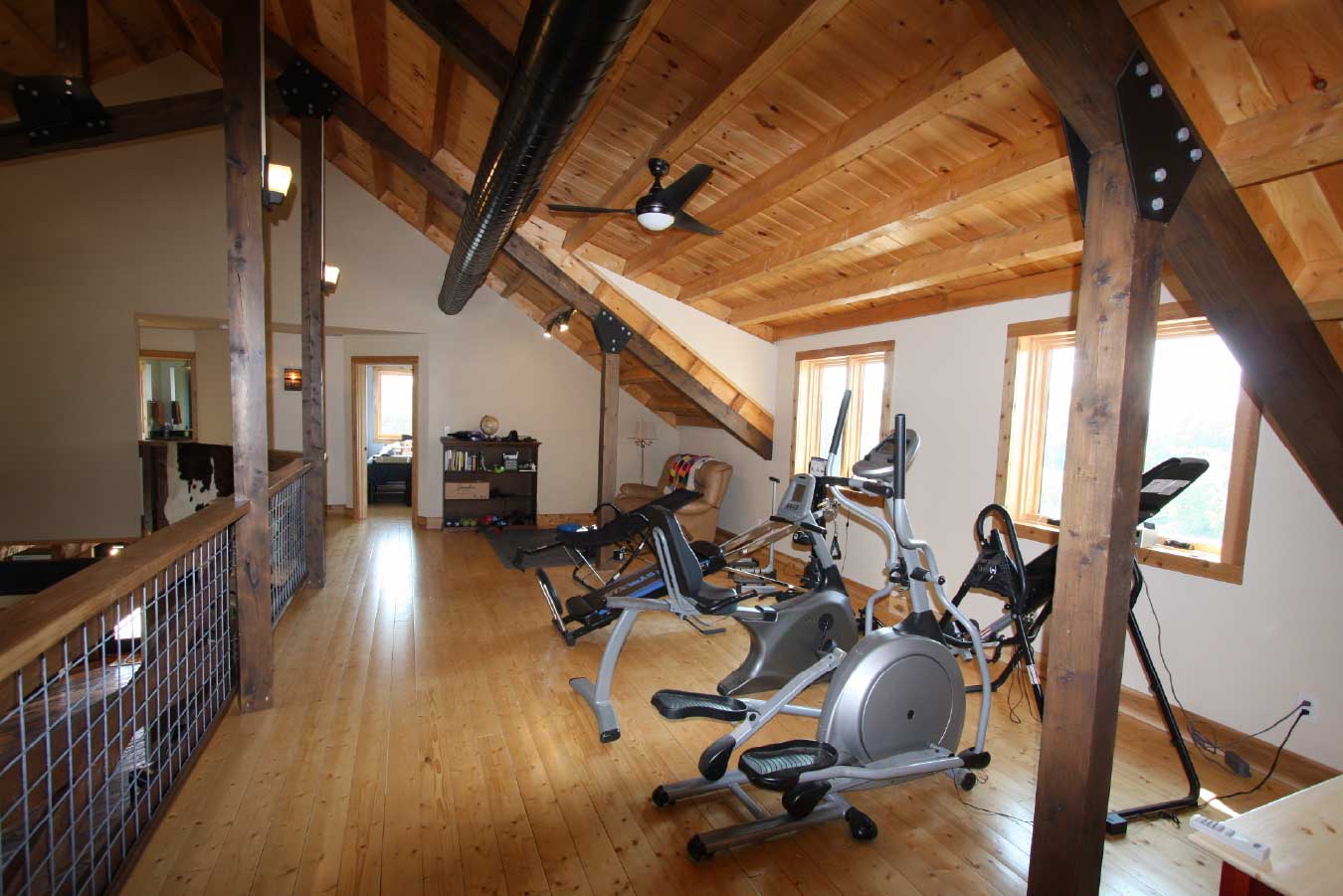 Loft fitness area inside a luxury timber frame home with exercise equipment, exposed wood beams, and a vaulted wood ceiling.
