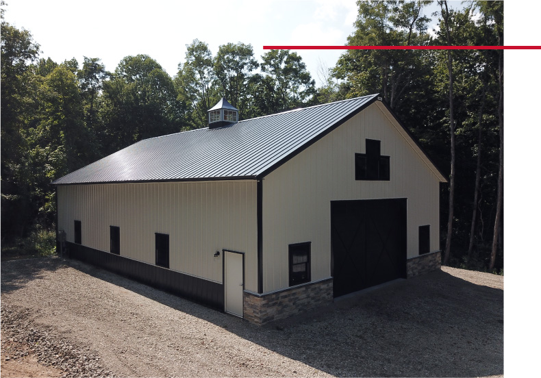 Front view of pole barn with black overhead doors, gable windows, white siding, and stone wainscot accents Front view of pole barn with black overhead doors, gable windows, white siding, and stone wainscot accents