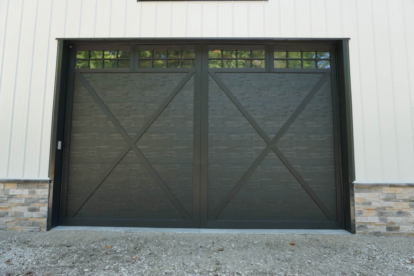 Front exterior of custom post-frame building with large black overhead door, cupola, and gravel driveway