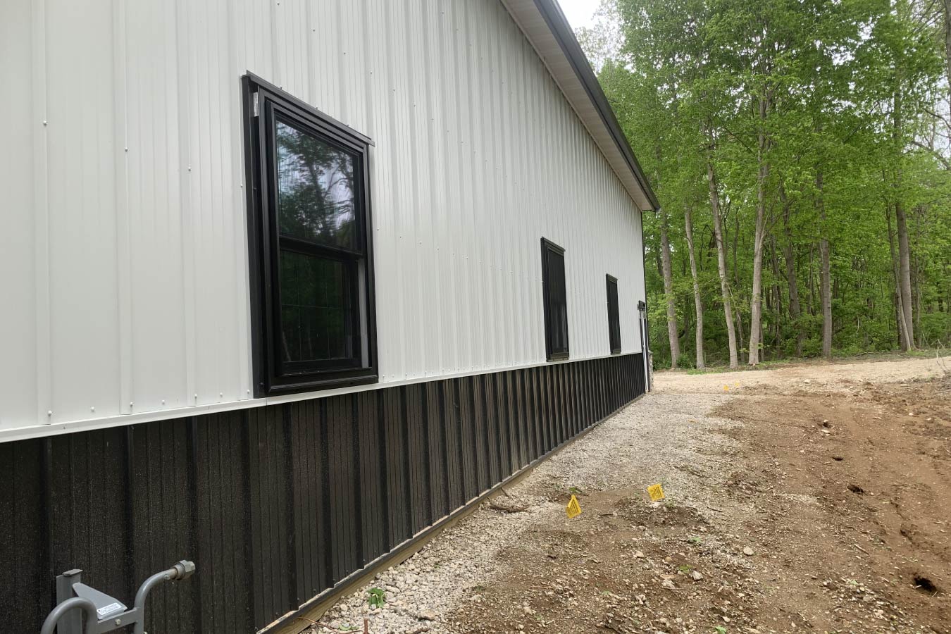 Exterior side view of post-frame building with white vertical metal siding, black trim, and dark wainscot