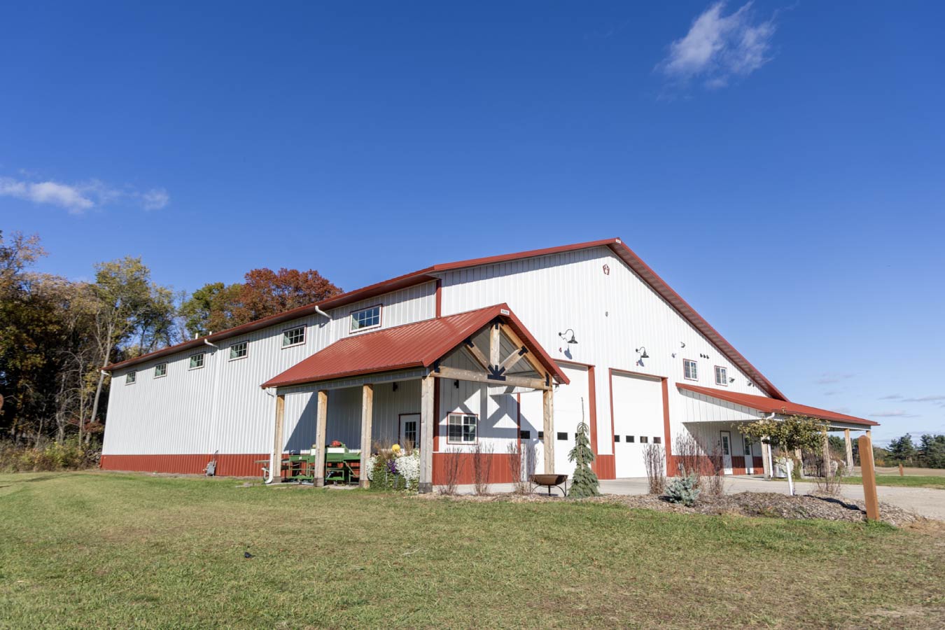 Front exterior with dual overhead doors, entry door, gooseneck lighting, and red roof on white steel siding