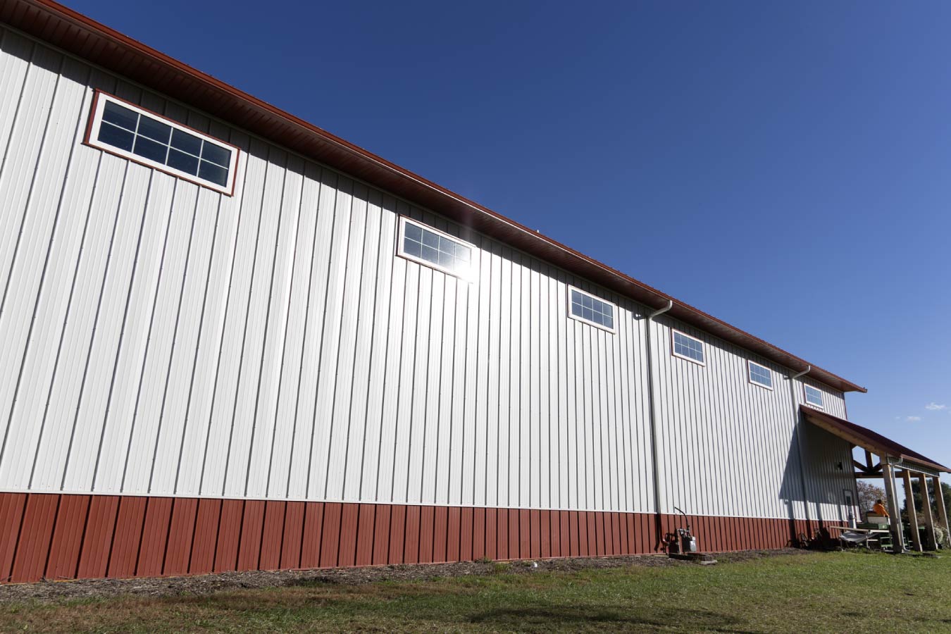 Side elevation of post-frame building with clerestory windows, white steel siding, and red wainscot for natural light