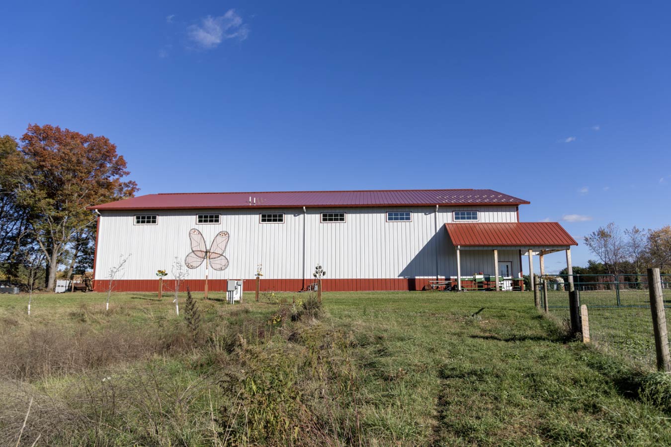 Exterior view of farm market building with wraparound covered porch, outdoor seating, and white steel siding with red wainscot