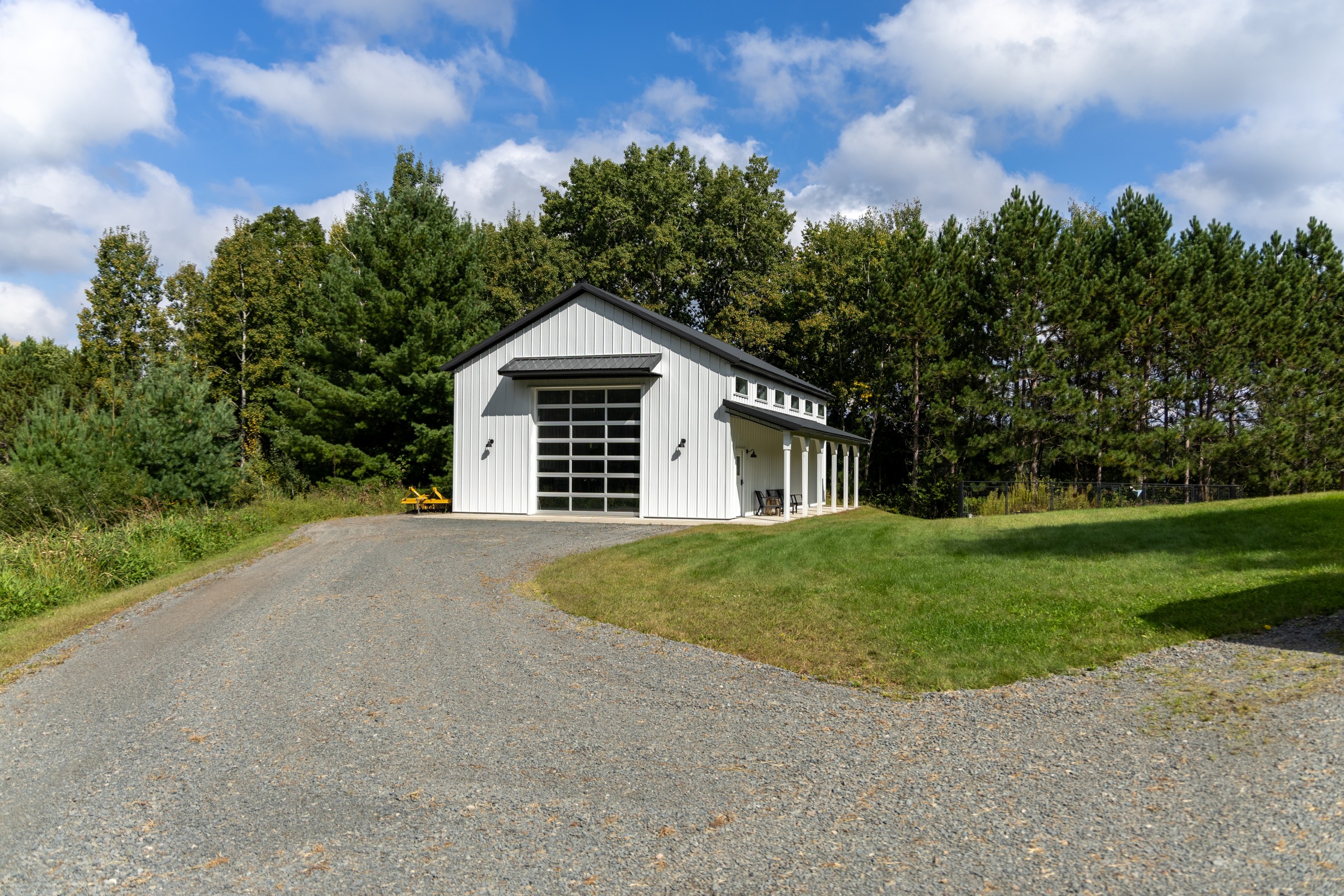30' x 48' pole barn garage on a rural property with white steel siding, black roof, side porch, and custom overhead door
