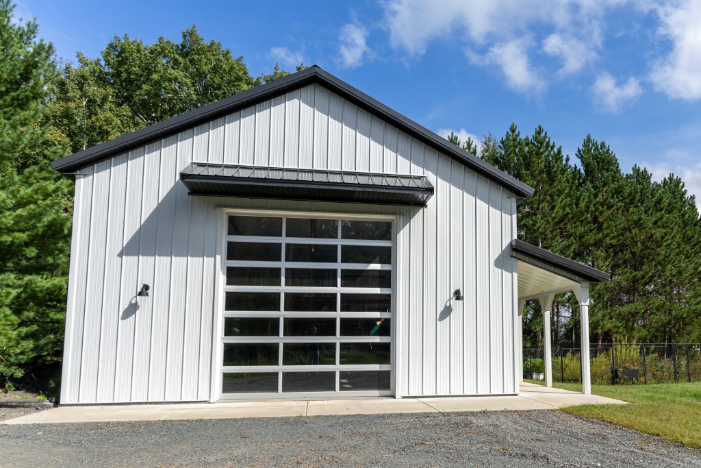 30' x 48' pole barn garage front with eyebrow overhang, white steel siding, black trim, and glass C.H.I. overhead door