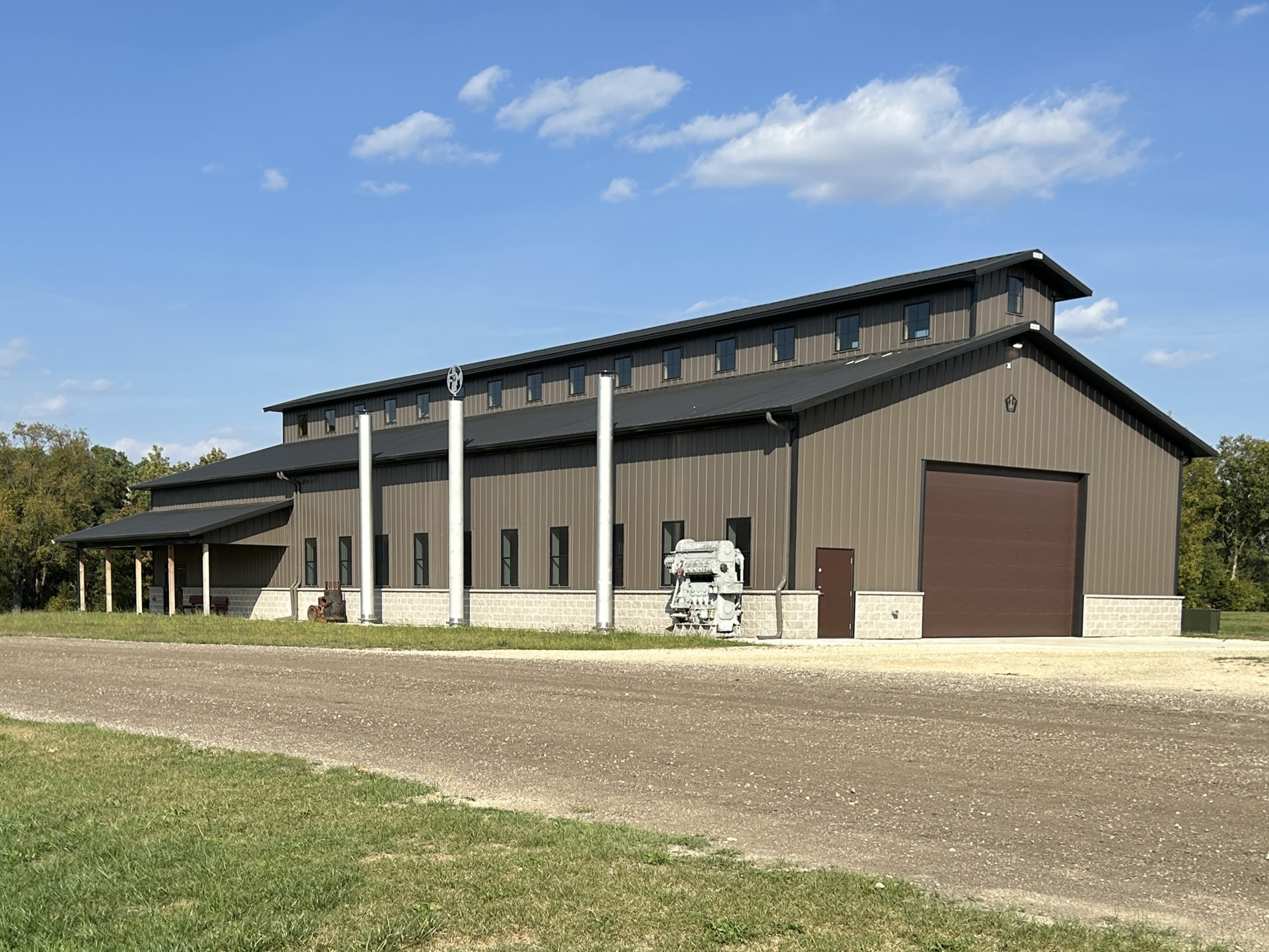 Baer Powerhouse at Rock River Thresheree, a 48′ × 124′ monitor-style commercial post-frame building with bronze siding, black roof, and stone wainscot.
