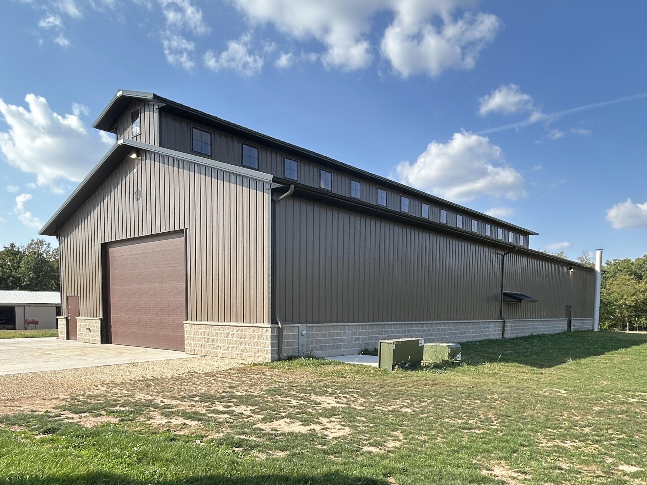 Side view of the Baer Powerhouse monitor-style pole barn with bronze steel siding, black roof, stone wainscot, and 20′ × 14′ overhead door.
