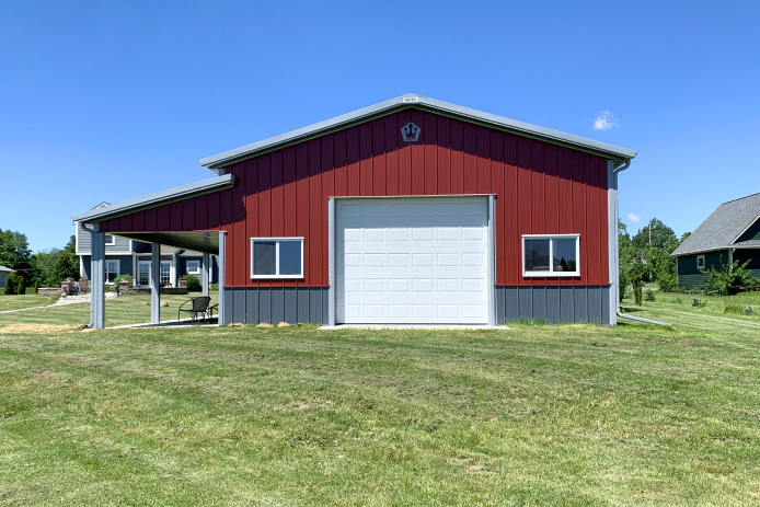 30×40 Pole Barn Garage Front View | Red Hobby Garage | Walters Buildings 30x40 red pole barn garage with white overhead door covered porch and gray wainscot steel siding