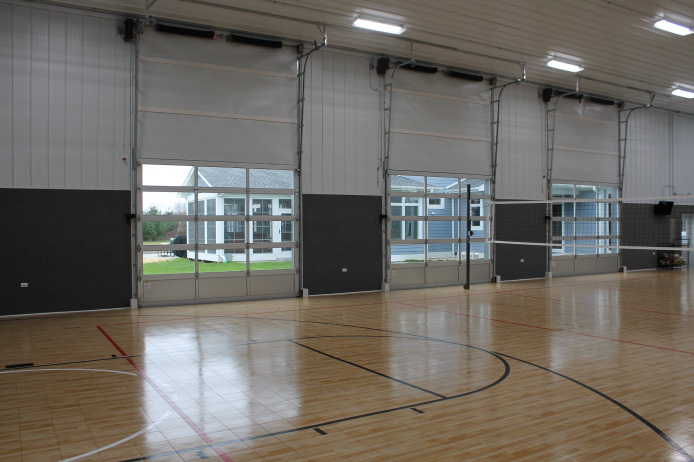Interior basketball court with hardwood flooring, high ceilings, and overhead doors inside post-frame building