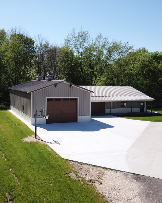 L shaped pole barn garage with brown steel siding, cupolas, covered porch, and oversized overhead garage door