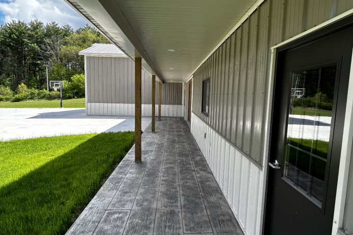 L shaped pole barn garage with covered porch, stamped concrete walkway, and black entry doors