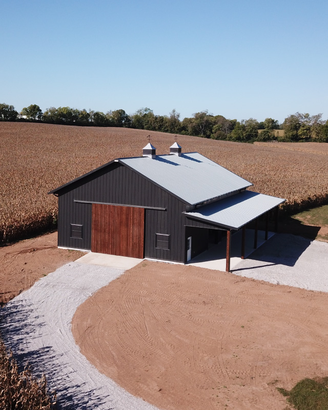 40×64 Pole Barn with Sliding Doors and Lean-To | Walters Buildings 40x64 pole barn with black steel siding, wood sliding doors, cupolas, and covered lean-to