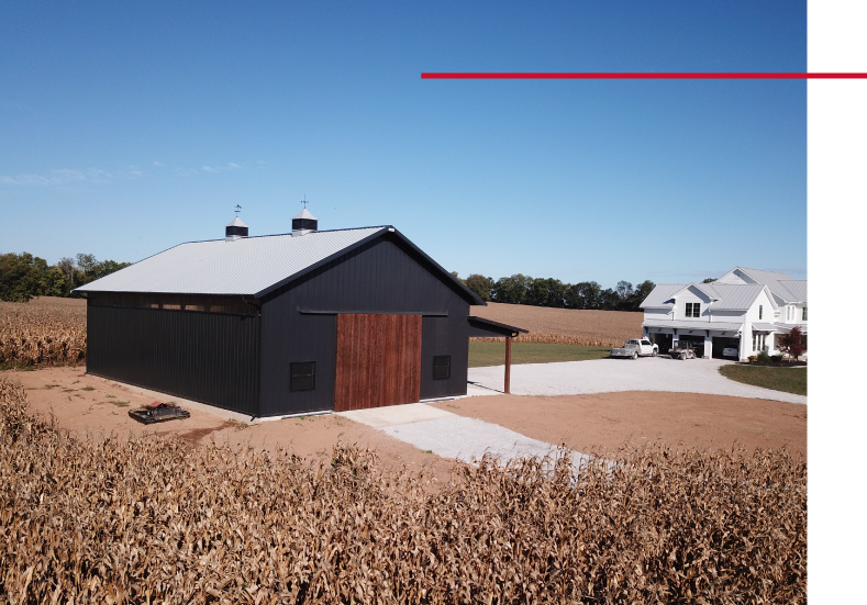 Exterior view of 40×64 pole barn with black siding, wood sliding doors, and lean-to addition in rural residential setting Exterior view of 40x64 pole barn with black siding, wood sliding doors, and lean-to addition in rural residential setting