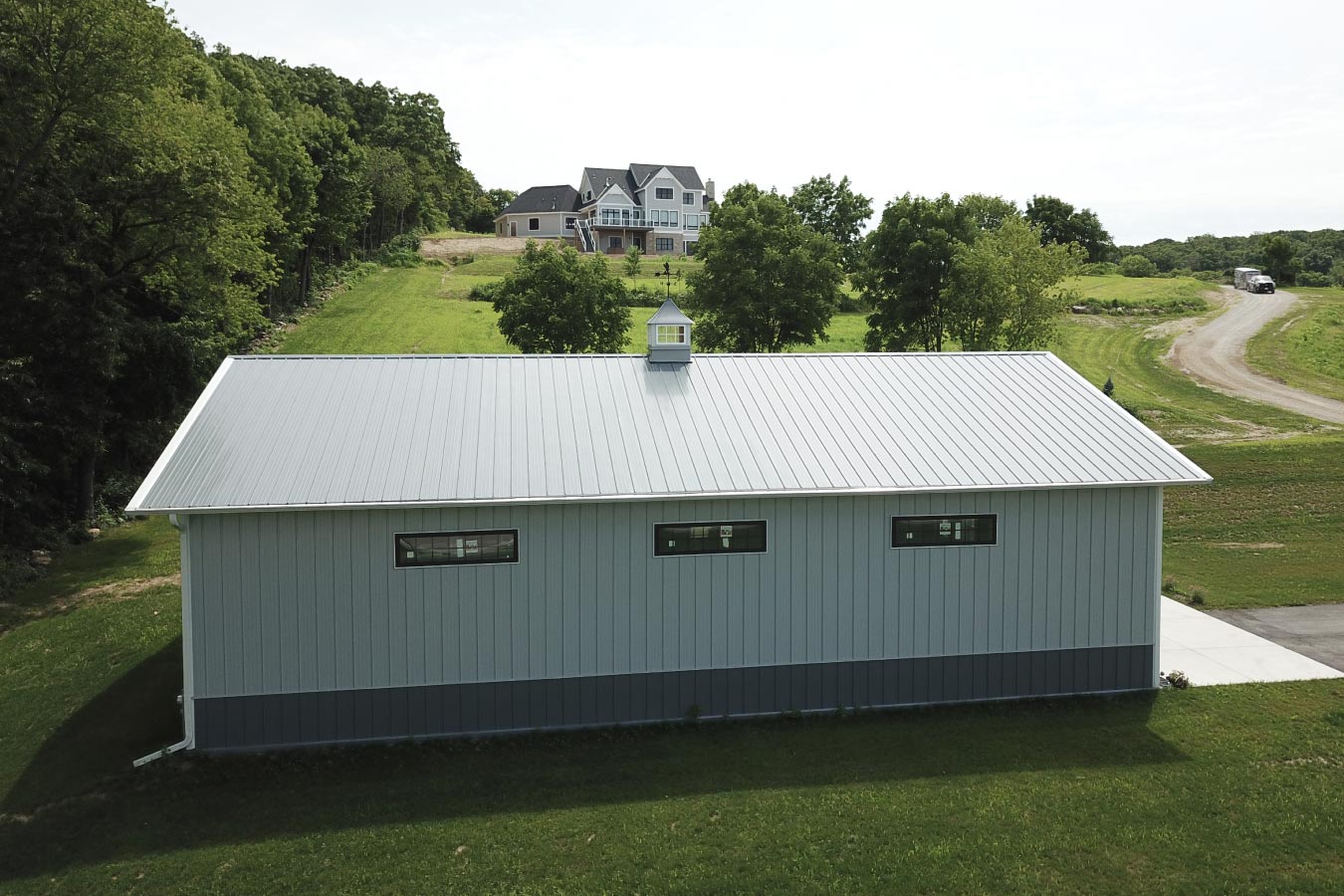 Side elevation of post-frame auto workshop with horizontal windows and metal roof on landscaped residential lot