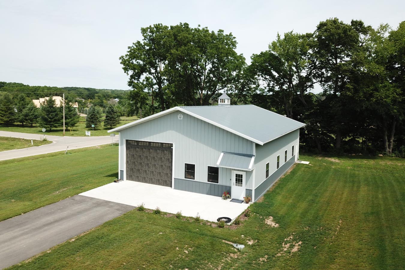 Angled front view of gray workshop building with overhead garage door, entry door, and concrete apron