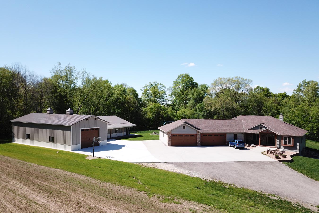 L shaped pole barn garage beside custom home with brown steel siding and large concrete driveway