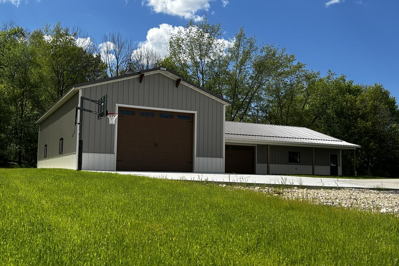 L shaped pole barn garage with brown steel siding, oversized garage door, and backyard basketball hoop