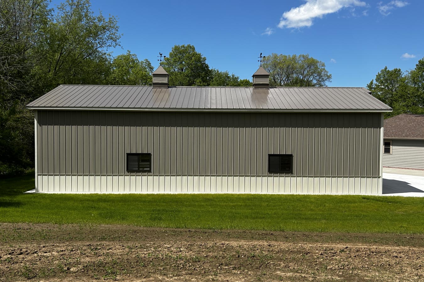 60x80 L shaped pole barn with gray steel siding, white wainscot, black windows, and decorative cupolas