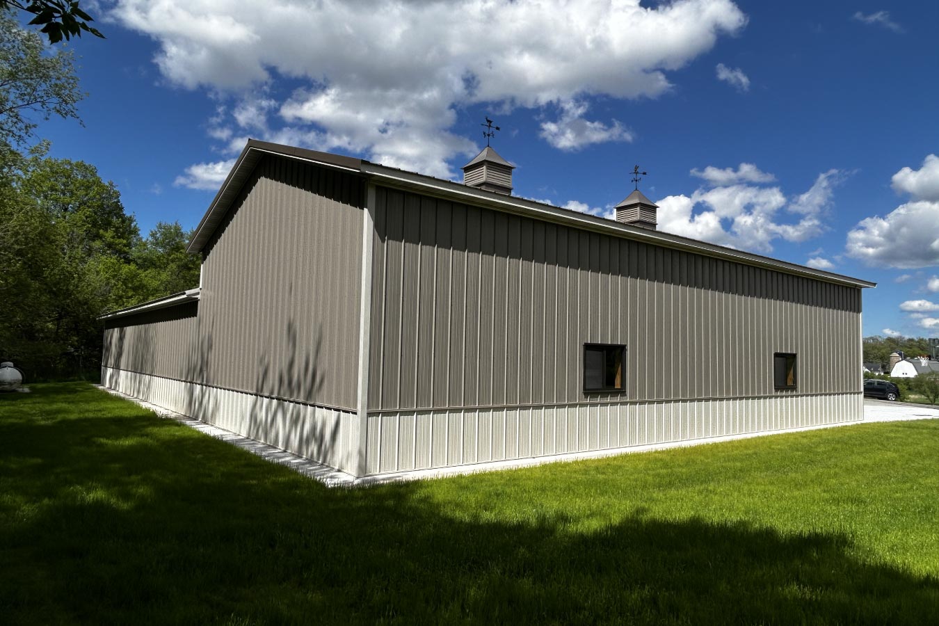 60x80 L shaped pole barn with gray steel siding, white wainscot, black windows, and decorative cupolas