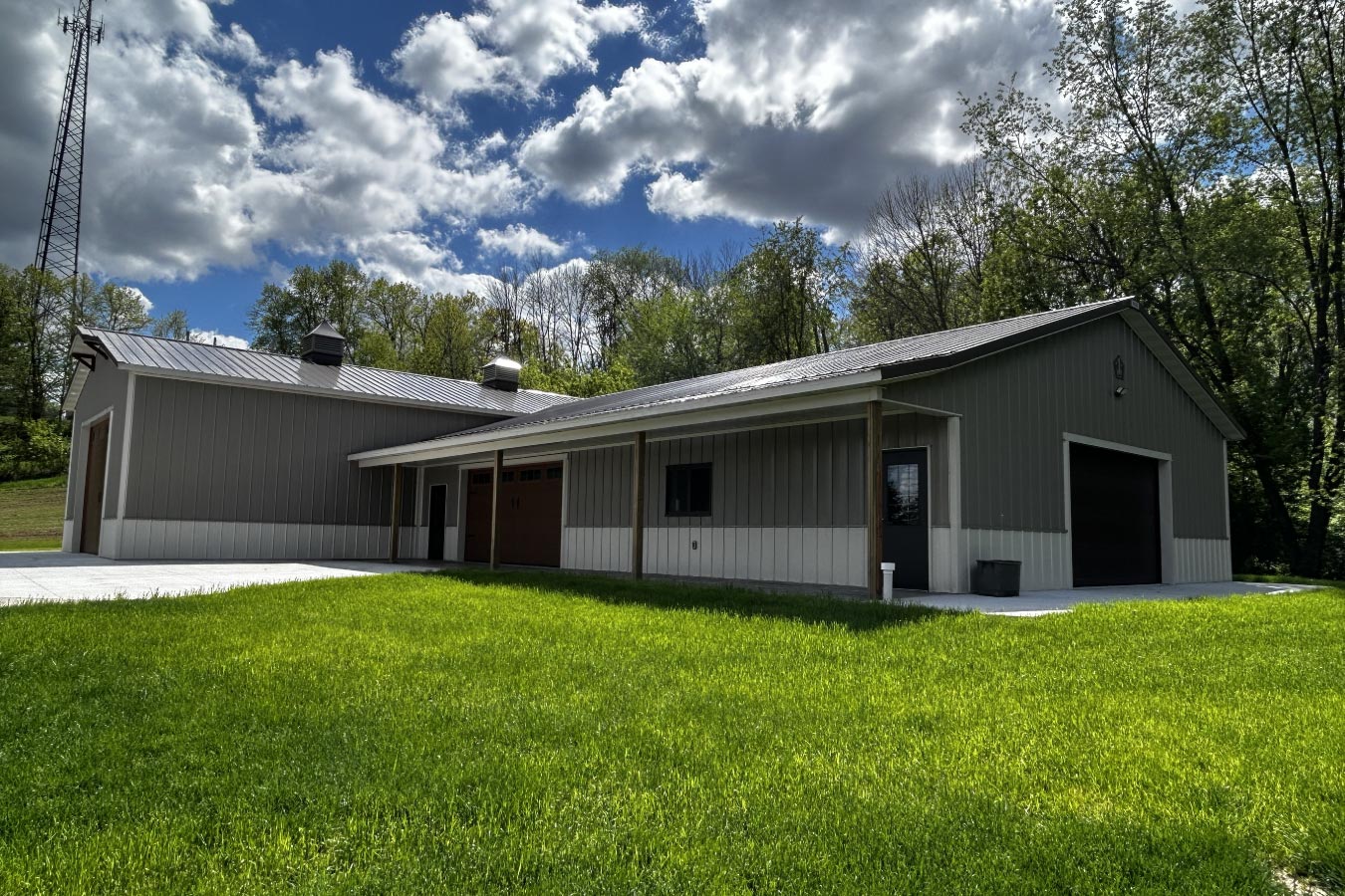 L shaped pole barn garage with covered workspace, multiple overhead doors, and gray steel siding