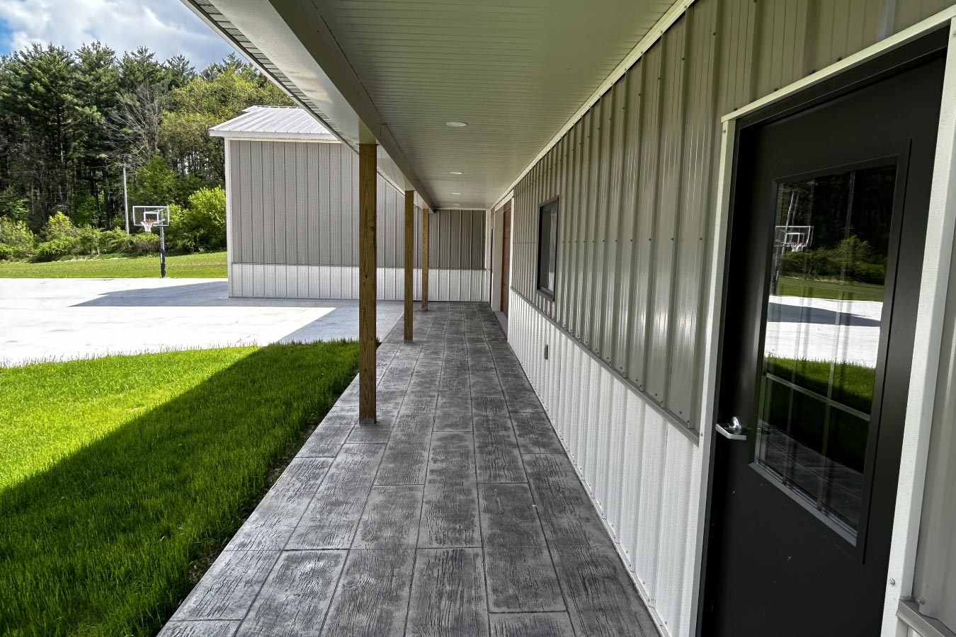 L shaped pole barn garage with covered porch, stamped concrete walkway, and black entry doors Covered breezeway wall